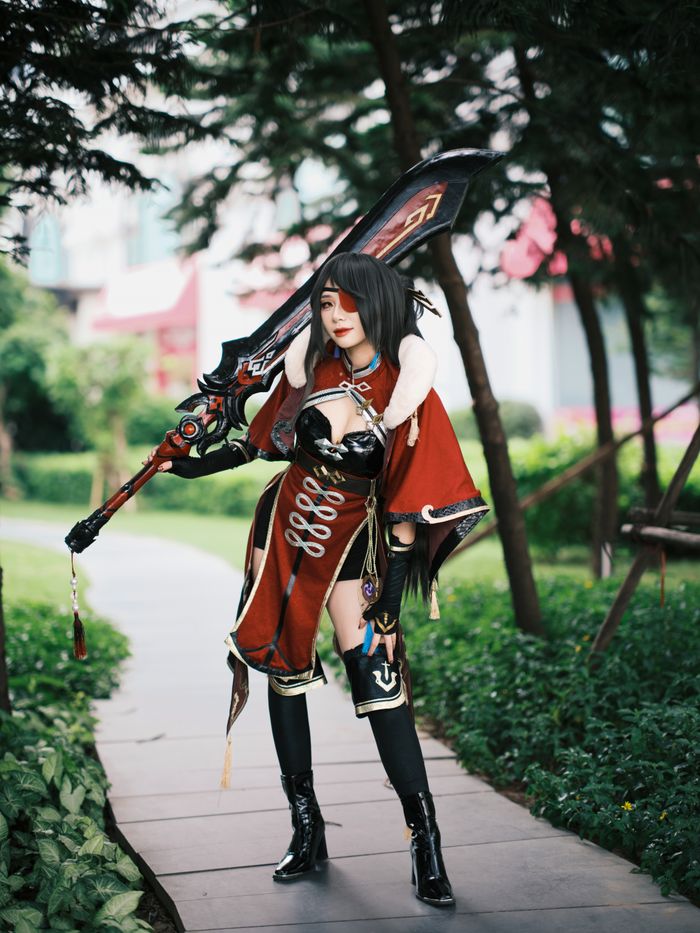 Cosplayer in detailed red costume holding a large sword in a lush outdoor setting.